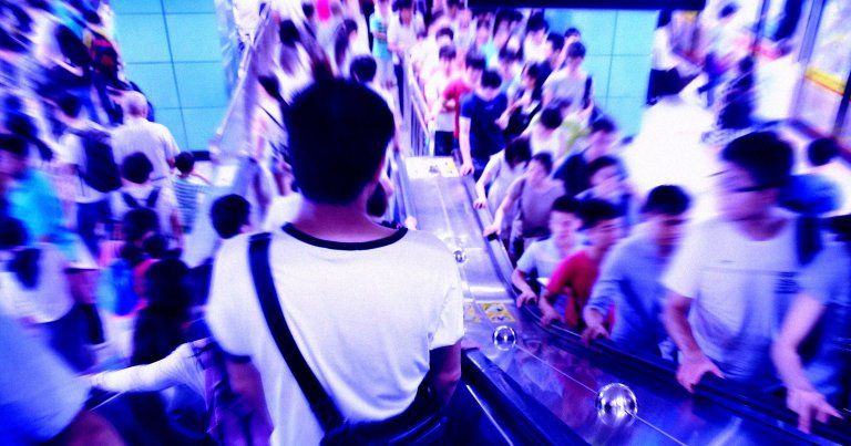A color-treated photo of a man using an escalator at a busy station.