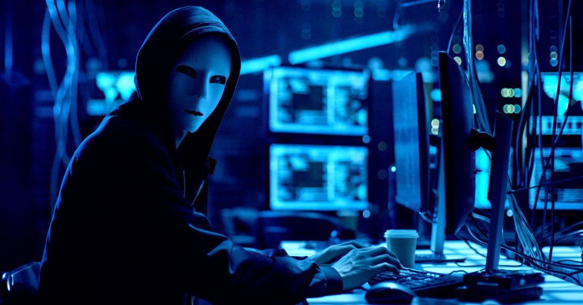 A hacker in front of an elaborate computer set up wearing a mask.
