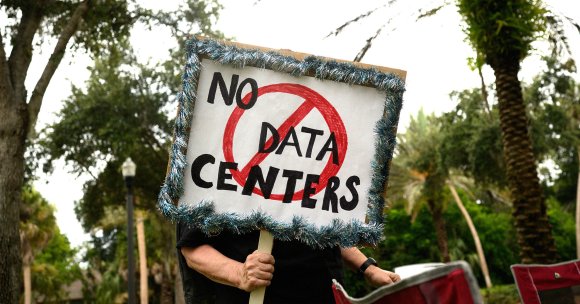 A person holds signs during a nationwide protest against AI data center expansion outside Peace Hall in New Port Richey, Florida. 