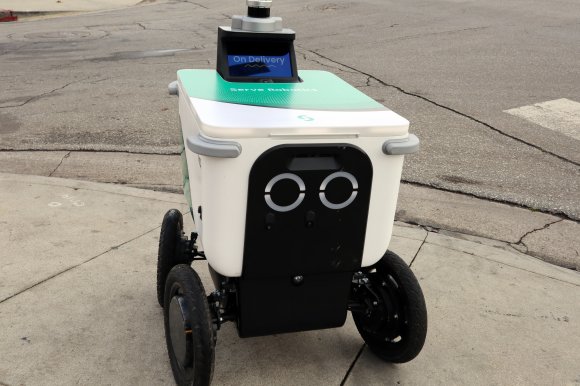 A Serve delivery robot is shown navigating a sidewalk.
