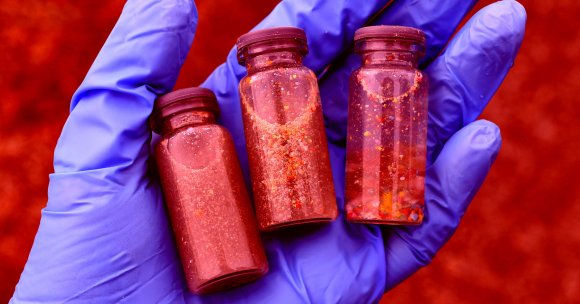 A hand holding vials of sand and microplastics.