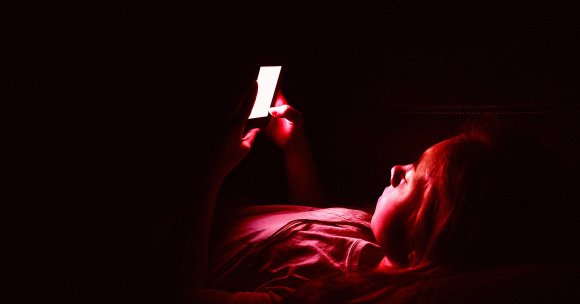 A girl lying down on a couch in the dark while using her smartphone.