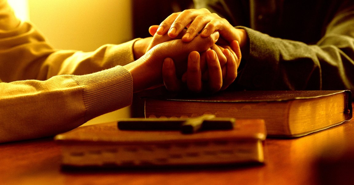 Two pairs of hands clasped over a bible.