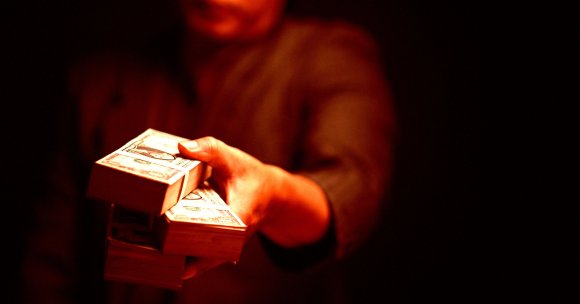 A business man handing over stacks of dollar bills.