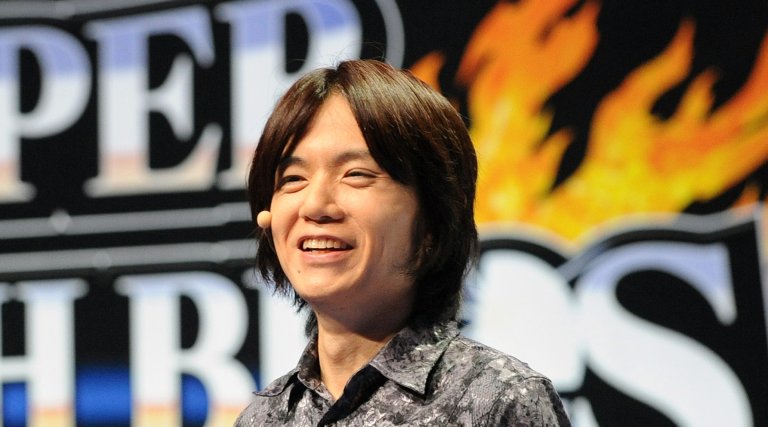 A photo shows Masahiro Sakurai in front of a banner for Super Smash Brothers.
