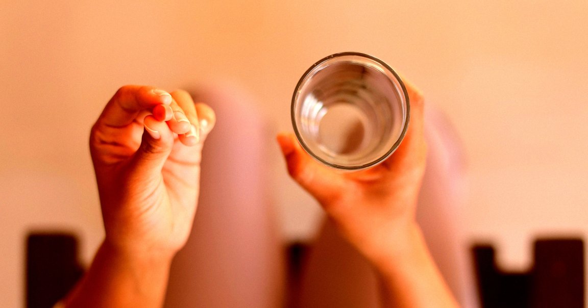 A woman taking a pill with a glass of water.