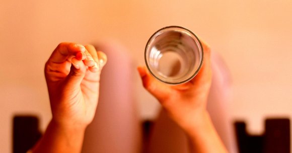 A woman taking a pill with a glass of water.